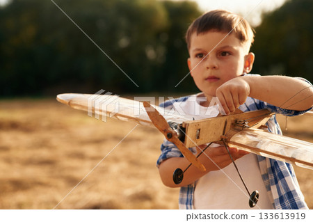 Boy is playing with wooden toy plane outdoors on the field Boy is playing with wooden toy plane outdoors on the field 133613919