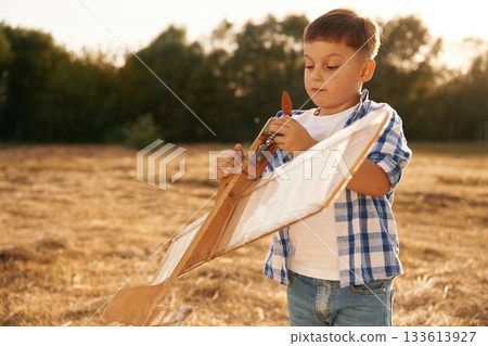 Fixing the toy. Boy is playing with wooden plane outdoors on the field Fixing the toy. Boy is playing with wooden plane outdoors on the field 133613927