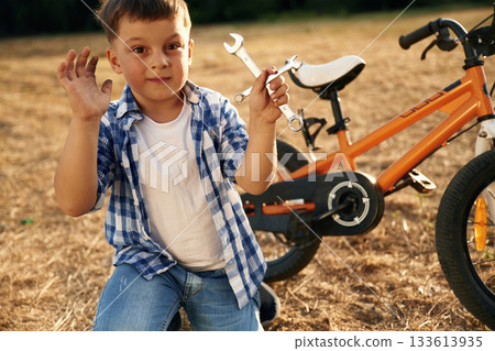 Repairing the bike, holding wrench. Cute boy is with his bicycle on the field 133613935