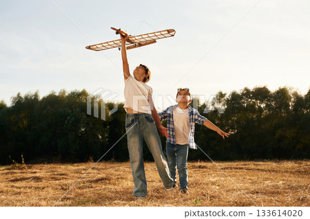 Having fun. Boy and girl are playing with wooden toy plane on the field Having fun. Boy and girl are playing with wooden toy plane on the field 133614020