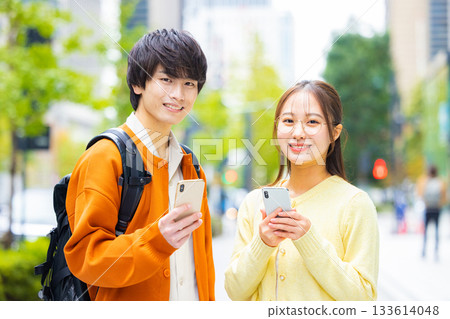 Young men and women looking at smartphones in the city Young men and women looking at smartphones in the city 133614048