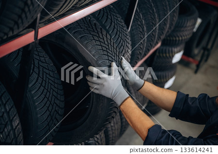 Close up view, taking the tire. Man worker is maintenance station with wheels 133614241