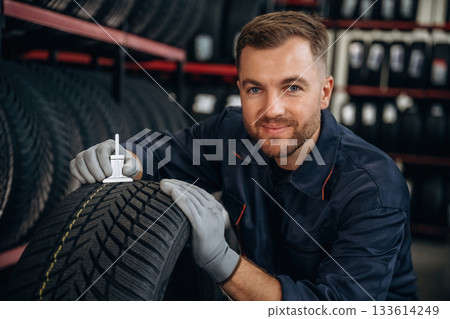 Tool for measuring. Man worker is maintenance station with tires, wheels Tool for measuring. Man worker is maintenance station with tires, wheels 133614249