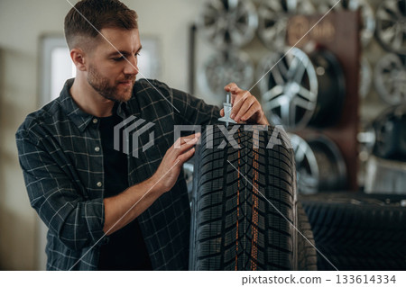 With measuring tool. Man worker is maintenance station with tires, wheels 133614334