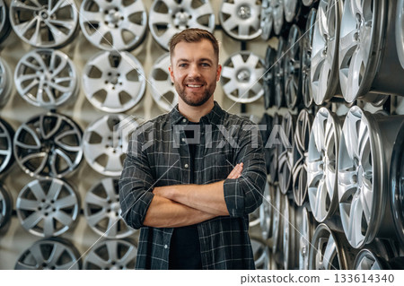 Standing with arms crossed. Man worker is maintenance station with tires, wheels 133614340