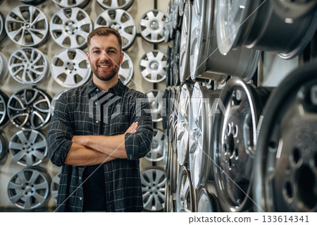 Standing with arms crossed. Man worker is maintenance station with tires, wheels 133614341