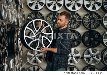 Brand new disk. Man worker is maintenance station with tires, wheels 133614353