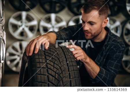 Sitting, professional man worker is maintenance station with tires, wheels 133614369