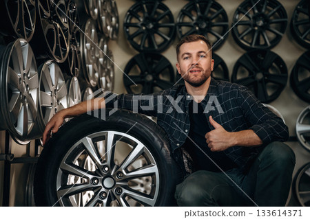 Thumb up, gesture. Man worker is maintenance station with tires, wheels 133614371
