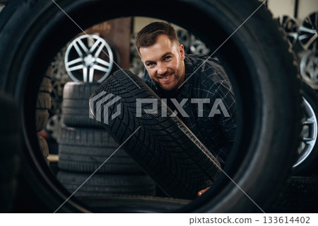 Looking through the hole in tire. Man worker is maintenance station with wheels Looking through the hole in tire. Man worker is maintenance station with wheels 133614402
