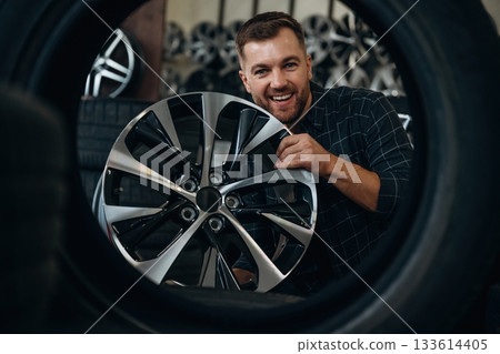 Brand new disk. Man worker is maintenance station with tires, wheels Brand new disk. Man worker is maintenance station with tires, wheels 133614405