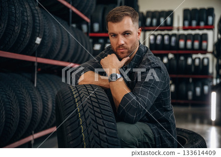 Thinking, sitting. Man worker is maintenance station with tires, wheels Thinking, sitting. Man worker is maintenance station with tires, wheels 133614409
