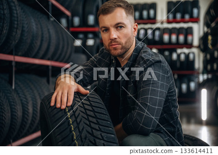 Thinking, sitting. Man worker is maintenance station with tires, wheels Thinking, sitting. Man worker is maintenance station with tires, wheels 133614411