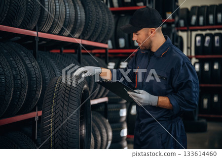 Black colored notepad, information, documents. Man worker is maintenance station with tires, wheels Black colored notepad, information, documents. Man worker is maintenance station with tires, wheels 133614460