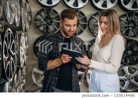 Male worker with woman in the car maintenance room, holding digital tablet, reading it Male worker with woman in the car maintenance room, holding digital tablet, reading it 133614490