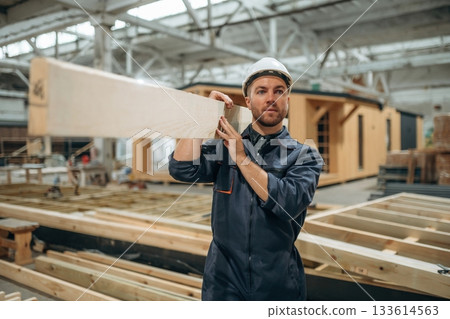 Wooden plank in hands. Male builder is at construction of house Wooden plank in hands. Male builder is at construction of house 133614563
