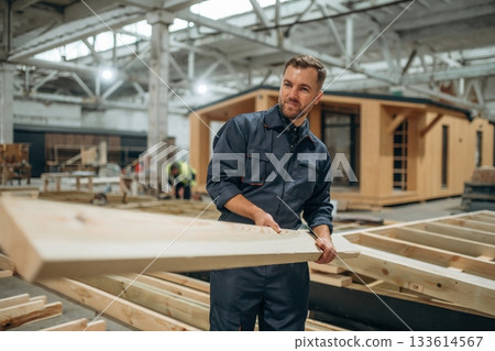 Wooden plank in hands. Male builder is at construction of house 133614567