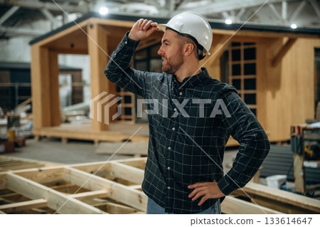 Looks far away. Male builder is at construction of wooden house Looks far away. Male builder is at construction of wooden house 133614647