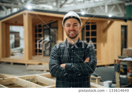 Cheerful facial expression. Male builder is at construction of wooden house Cheerful facial expression. Male builder is at construction of wooden house 133614649
