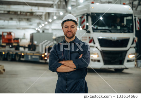 Standing in front of a truck. Male worker is in the modern warehouse or manufacturing company Standing in front of a truck. Male worker is in the modern warehouse or manufacturing company 133614666