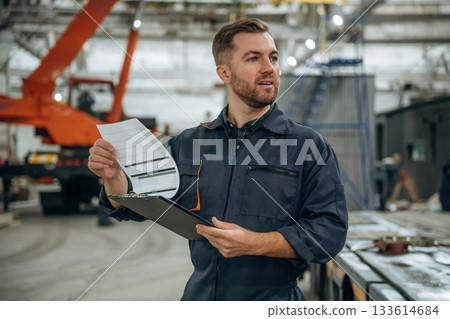 Front view, holding notepad, standing. Male worker is in the modern warehouse or manufacturing company 133614684