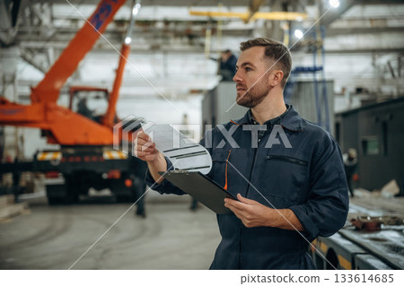 Front view, holding notepad, standing. Male worker is in the modern warehouse or manufacturing company Front view, holding notepad, standing. Male worker is in the modern warehouse or manufacturing company 133614685