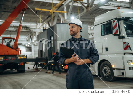 Front view, holding notepad, standing. Male worker is in the modern warehouse or manufacturing company 133614688