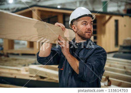 The plank, man is holding it. Male builder is at construction of wooden house 133614703