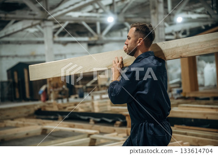 The plank, man is holding it. Male builder is at construction of wooden house The plank, man is holding it. Male builder is at construction of wooden house 133614704
