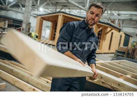 The plank, man is holding it. Male builder is at construction of wooden house The plank, man is holding it. Male builder is at construction of wooden house 133614705