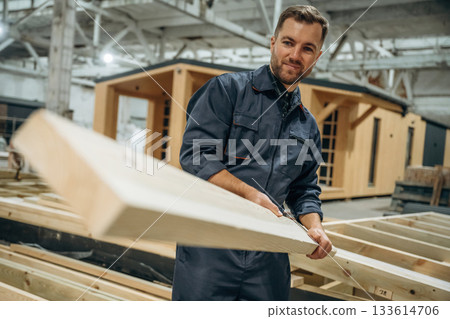 The plank, man is holding it. Male builder is at construction of wooden house The plank, man is holding it. Male builder is at construction of wooden house 133614706