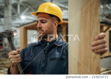 Plank and a hammer. Male builder is at construction of wooden house 133614711