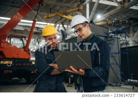 Reading information from laptop. Two male factory workers are in the warehouse 133614727