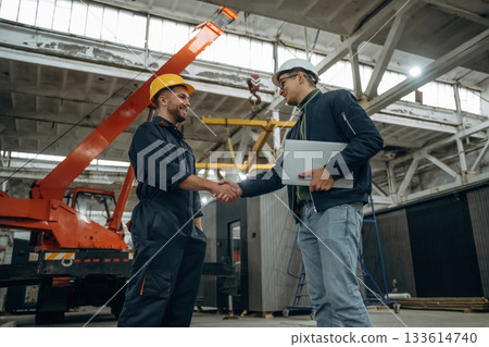 Friendly handshake. Two male factory workers are in the warehouse Friendly handshake. Two male factory workers are in the warehouse 133614740