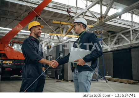 Friendly handshake. Two male factory workers are in the warehouse Friendly handshake. Two male factory workers are in the warehouse 133614741