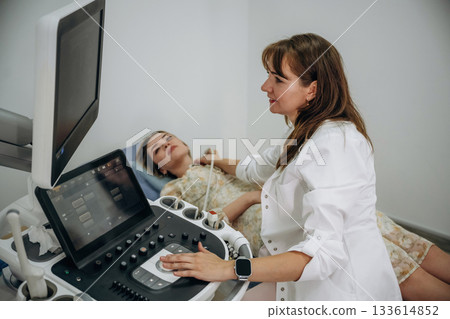 Woman is lying down and undergoing ultrasonic test of the thyroid gland Woman is lying down and undergoing ultrasonic test of the thyroid gland 133614852