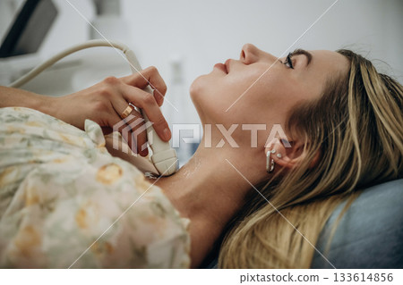 Woman is lying down and undergoing ultrasonic test of the thyroid gland Woman is lying down and undergoing ultrasonic test of the thyroid gland 133614856