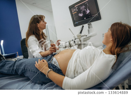 Monitor with graphical representation of scan. Pregnant woman undergoing ultrasound test Monitor with graphical representation of scan. Pregnant woman undergoing ultrasound test 133614889