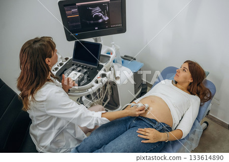 Monitor with graphical representation of scan. Pregnant woman undergoing ultrasound test 133614890