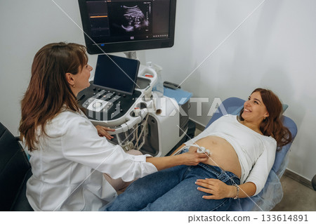 Monitor with graphical representation of scan. Pregnant woman undergoing ultrasound test Monitor with graphical representation of scan. Pregnant woman undergoing ultrasound test 133614891