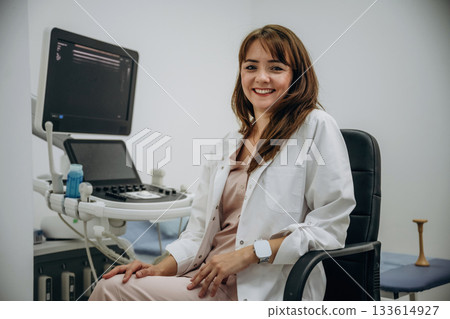 Sitting and smiling. Doctor is with ultrasound equipment is in the clinic in the room Sitting and smiling. Doctor is with ultrasound equipment is in the clinic in the room 133614927