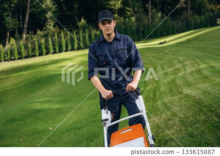 With lawn mover, working. Professional gardener is on the lawn With lawn mover, working. Professional gardener is on the lawn 133615087