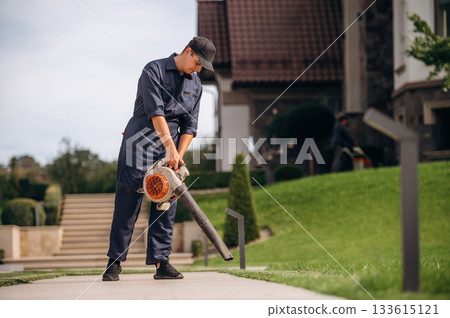 Leaf blower in hands, cleaning the way. Professional gardener is on the lawn Leaf blower in hands, cleaning the way. Professional gardener is on the lawn 133615121