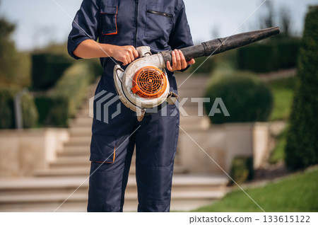 Professional leaf blower in hands of the gardener that is working on the lawn Professional leaf blower in hands of the gardener that is working on the lawn 133615122