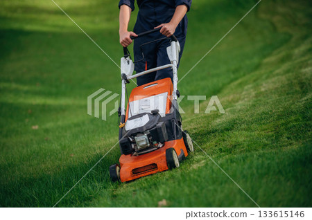 Process of cutting the grass by using lawn mover. Professional gardener is on the lawn 133615146