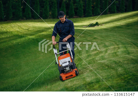 Process of cutting the grass by using lawn mover. Professional gardener is on the lawn 133615147
