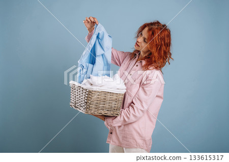 Basket with cleaned fresh clothes. Woman is in the studio against background Basket with cleaned fresh clothes. Woman is in the studio against background 133615317