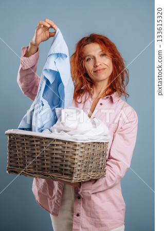 Basket with cleaned fresh clothes. Woman is in the studio against background 133615320