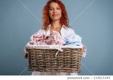 Front view. Holding bunch of fresh clothes, washed. Woman is in the studio against background Front view. Holding bunch of fresh clothes, washed. Woman is in the studio against background 133615345