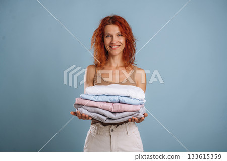 After the washing, holding fresh clothes. Woman is in the studio against background After the washing, holding fresh clothes. Woman is in the studio against background 133615359